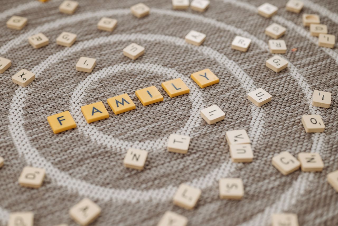 team-03 An artistic display of Scrabble tiles spelling 'FAMILY' on a textured carpet surface.